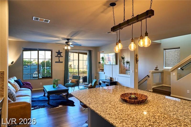 An open-concept living space boasts rich hardwood flooring, a spacious granite island, and abundant natural light from large windows and a balcony door.