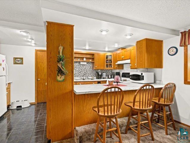 3616 Lavaque Road Hermantown, MN 55811 - Photo 36 of 43 Kitchen featuring wood-finish cabinetry, a patterned tile backsplash, and a breakfast bar with a light-toned countertop