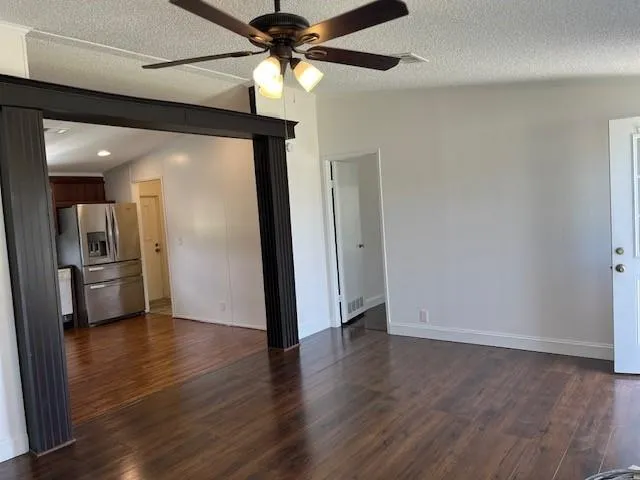 an empty room with wooden floor a ceiling fan and kitchen view