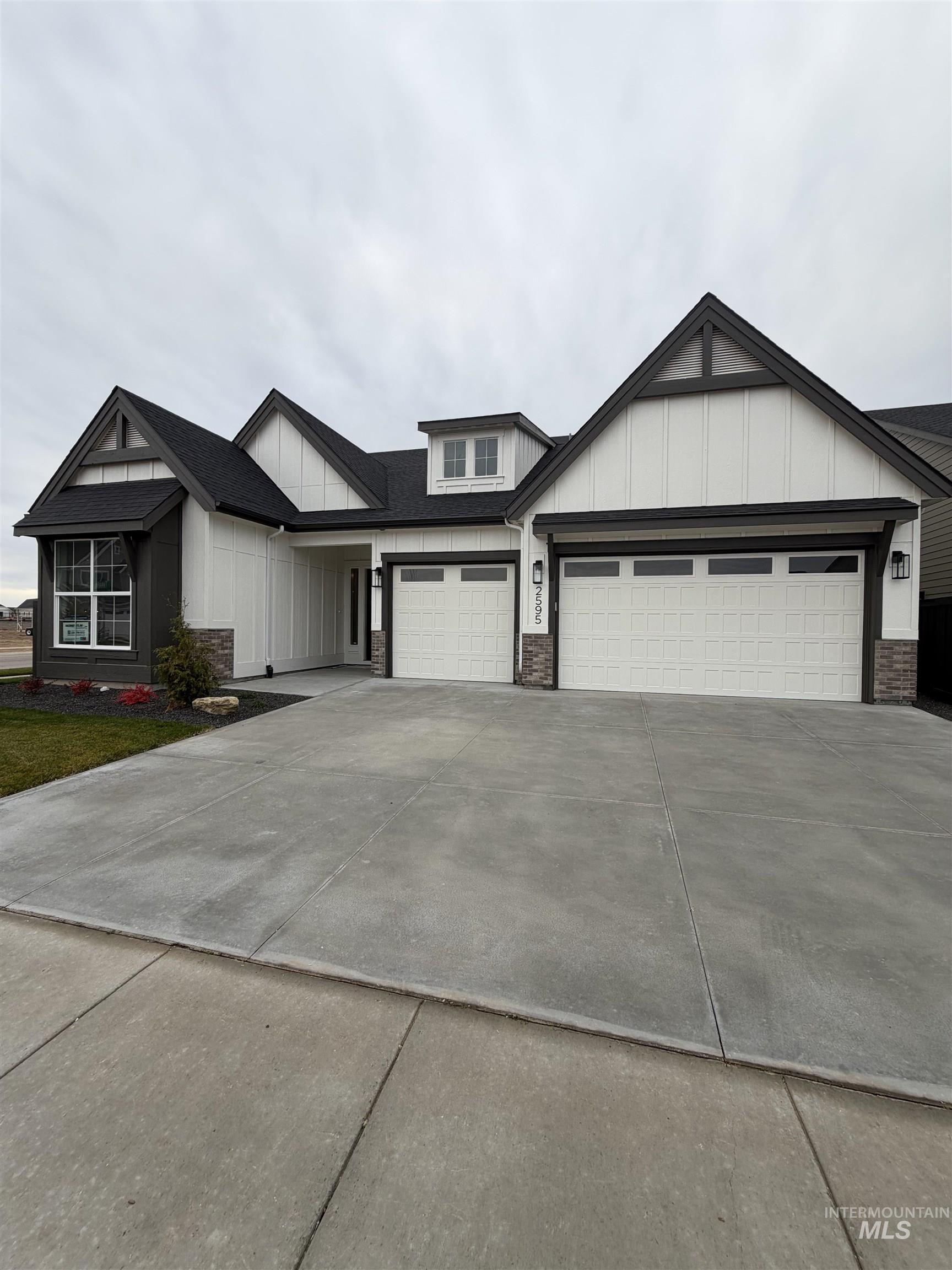 View of front facade featuring board and batten siding, driveway, and stone siding