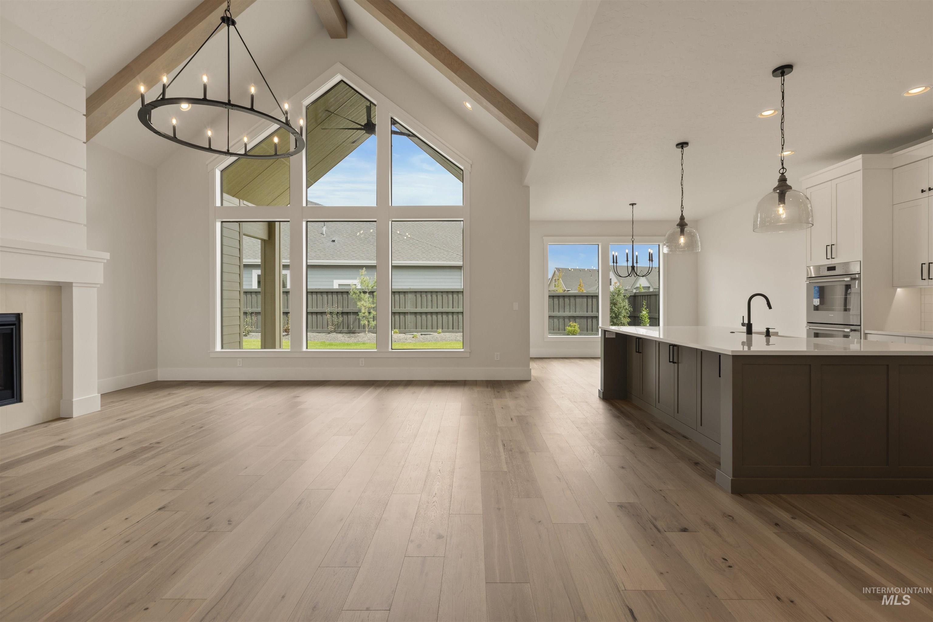 2595 East Tenzing Drive Meridian, ID 83642 - Photo 2 of 32 Unfurnished living room with a chandelier, beam ceiling, light wood finished floors, a tiled fireplace, and high vaulted ceiling