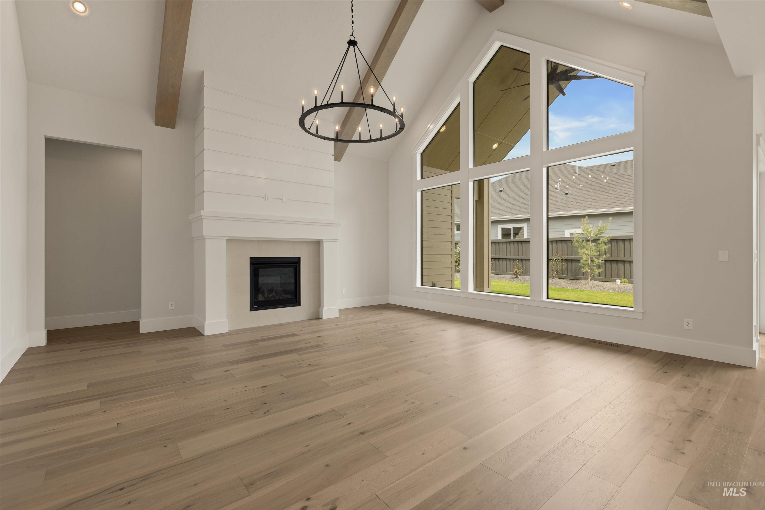 2595 East Tenzing Drive Meridian, ID 83642 - Photo 3 of 32 Unfurnished living room featuring high vaulted ceiling, beamed ceiling, a fireplace, light wood-type flooring, and a chandelier