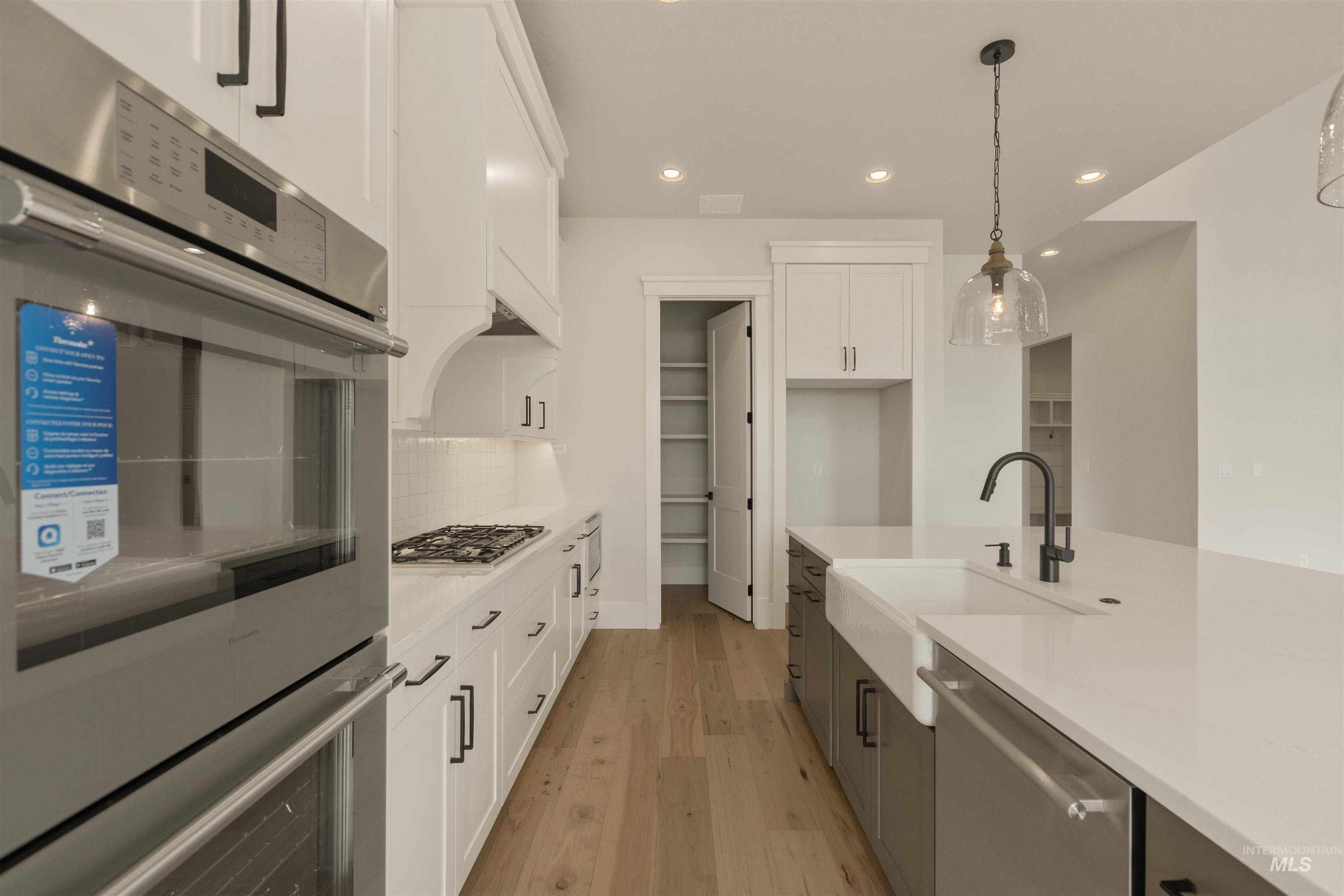 2595 East Tenzing Drive Meridian, ID 83642 - Photo 10 of 32 Kitchen with white cabinetry, appliances with stainless steel finishes, recessed lighting, hanging light fixtures, and light wood-type flooring