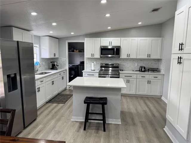 a kitchen with stainless steel appliances a microwave a sink a stove a refrigerator cabinets and wooden floor