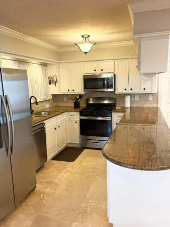 a kitchen with stainless steel appliances kitchen island granite countertop a sink a stove top oven and white cabinets