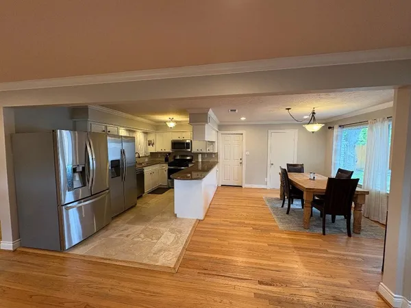 a large kitchen with stainless steel appliances kitchen island granite countertop a refrigerator a stove a dining table and chairs with wooden floor