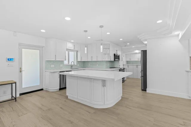 a large kitchen with kitchen island a sink dishwasher a refrigerator and white cabinets with wooden floor