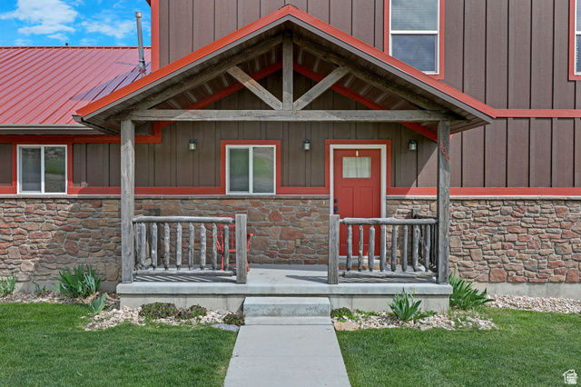 306 Spring Road Preston, ID 83263 - Photo 48 of 55 Inviting front entrance featuring a covered porch with log railings, stone facade, board and batten siding, a red metal roof, and a red entry door