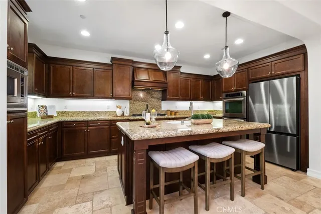 a kitchen with stainless steel appliances granite countertop a sink a stove a refrigerator and chairs