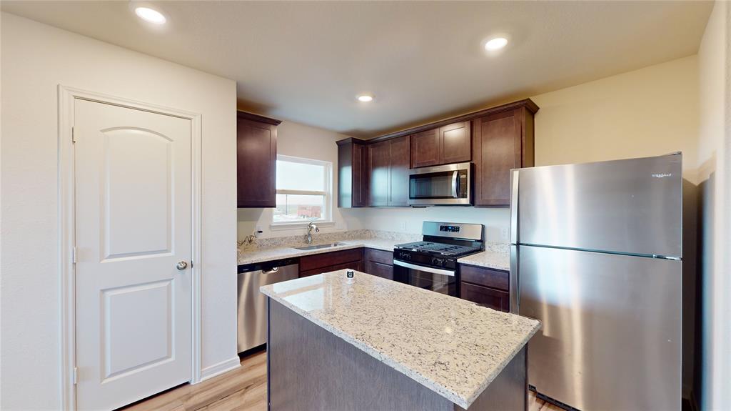 8012 White Sulphur Road Ponder, TX 76259 - Photo 21 of 39 Kitchen with stainless steel appliances, light stone countertops, a center island, dark brown cabinets, and light wood-type flooring