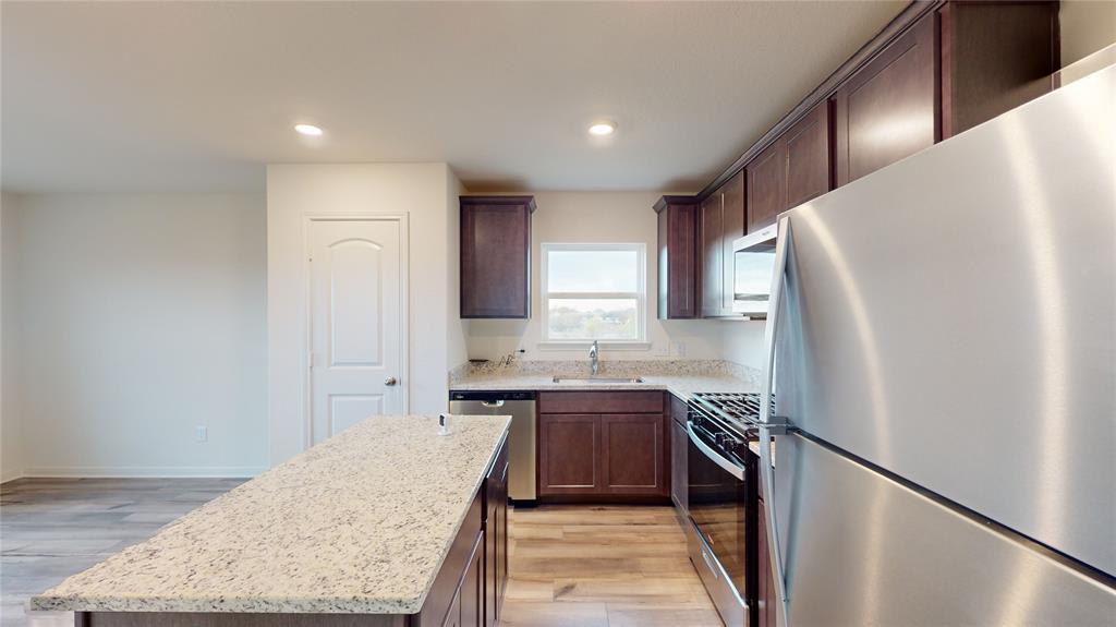 8012 White Sulphur Road Ponder, TX 76259 - Photo 23 of 39 Kitchen with appliances with stainless steel finishes, light wood-style floors, a kitchen island, light stone countertops, and dark brown cabinetry