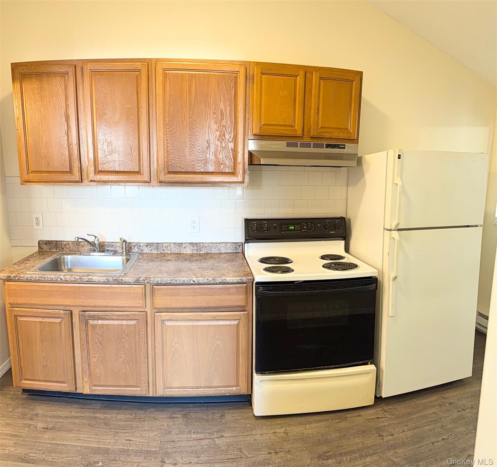188 Hallock Landing Road Rocky Point, NY 11778 - Photo 3 of 25 Kitchen featuring white appliances, under cabinet range hood, dark wood-style floors, decorative backsplash, and brown cabinets