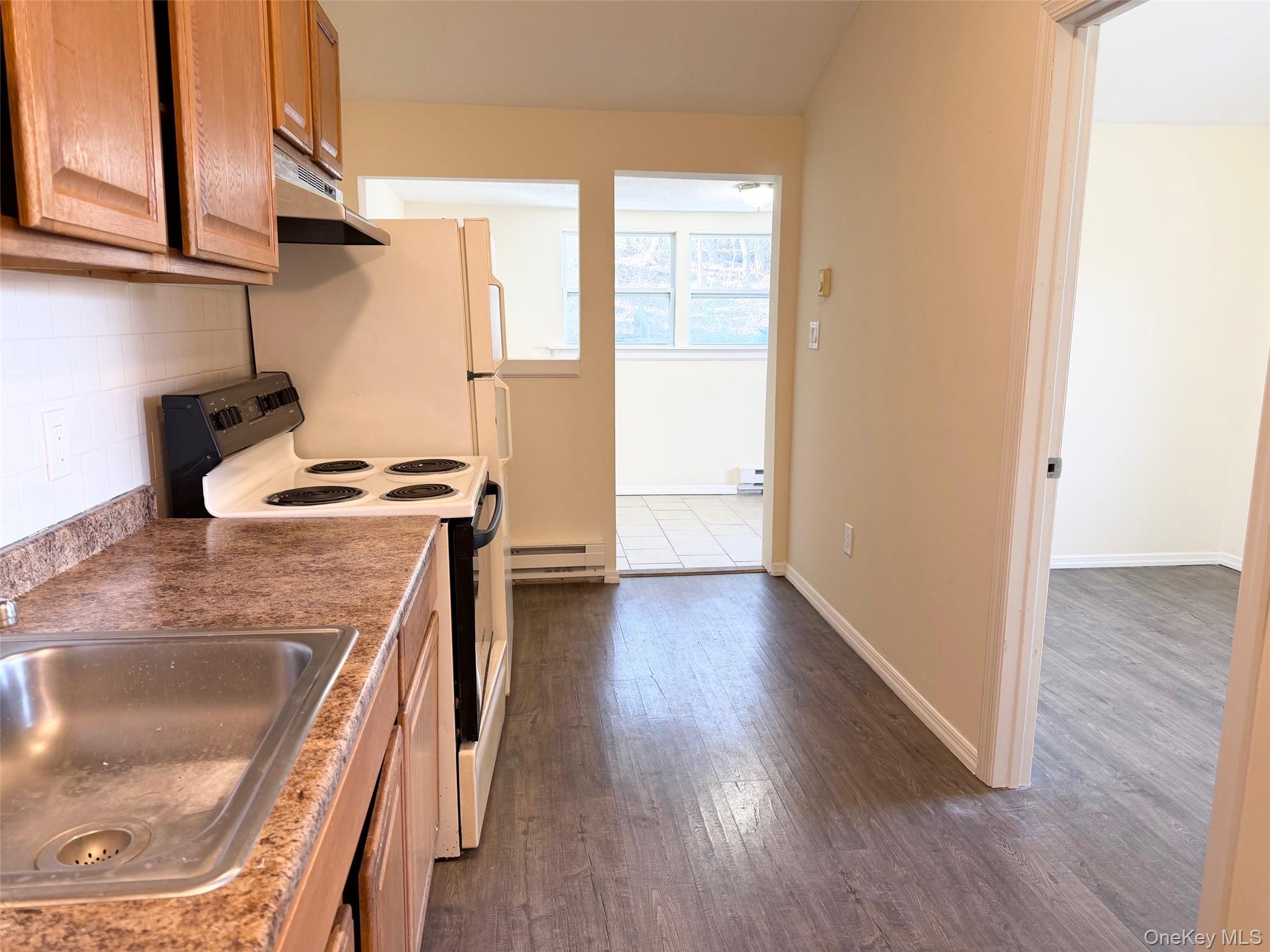 188 Hallock Landing Road Rocky Point, NY 11778 - Photo 5 of 25 Kitchen with white range with electric cooktop, dark wood-type flooring, under cabinet range hood, a baseboard heating unit, and tasteful backsplash