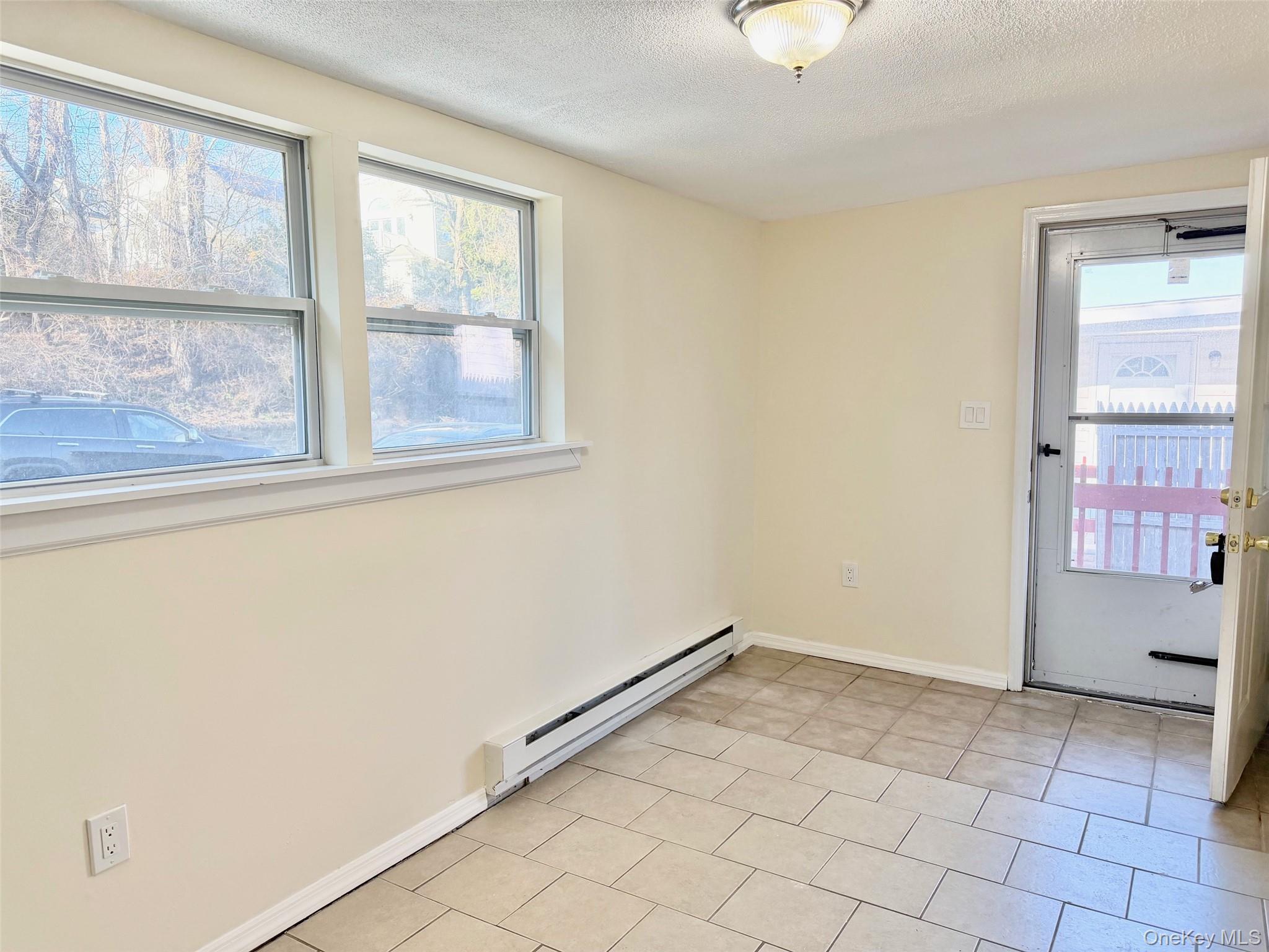 188 Hallock Landing Road Rocky Point, NY 11778 - Photo 7 of 25 Unfurnished room featuring baseboard heating, a textured ceiling, plenty of natural light, and light tile patterned floors
