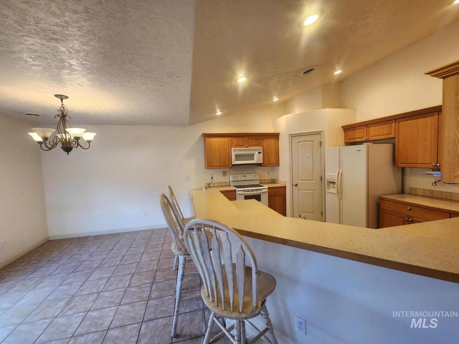 1000 North Rodeo Street Parma, ID 83660 - Photo 5 of 33 Kitchen featuring light countertops, white appliances, wood finish cabinets, hanging lights, and a breakfast bar