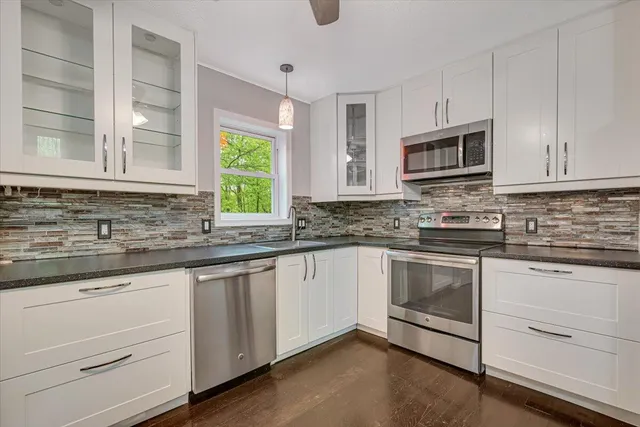 a kitchen with granite countertop white cabinets appliances a sink and a window