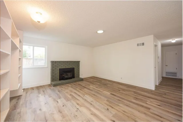 an empty room with wooden floor fireplace and windows