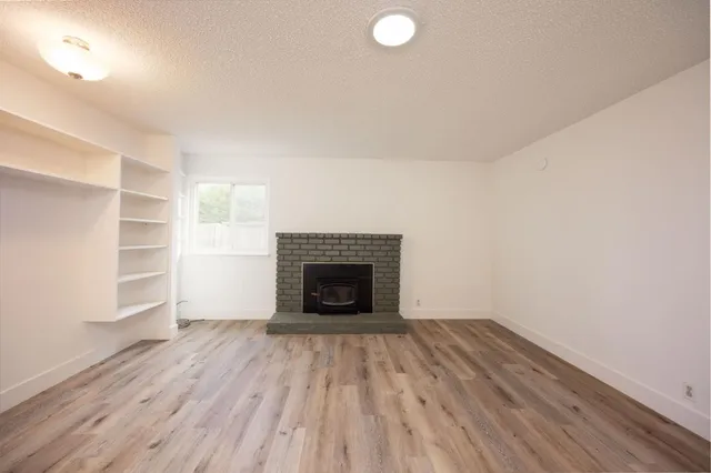 a view of an empty room with wooden floor fireplace and a window
