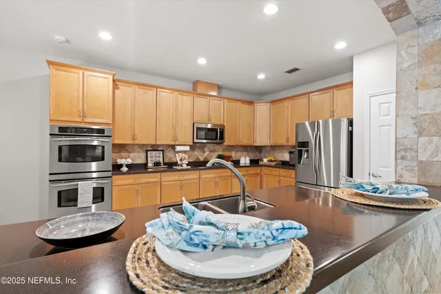 a kitchen with stainless steel appliances granite countertop a stove a sink a refrigerator and white cabinets with wooden floor