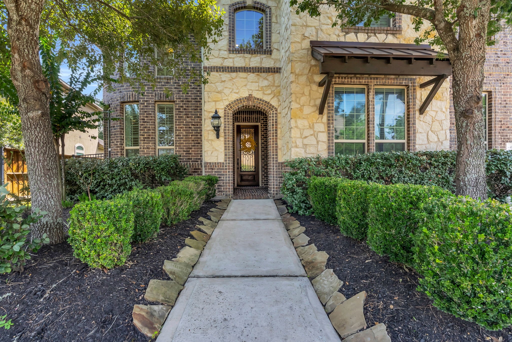 4022 Sabine Valley Trail Spring, TX 77386 - Photo 2 of 46 Grand entrance with a stone and brick facade, framed by manicured hedges and mature trees, leading to a welcoming arched doorway.