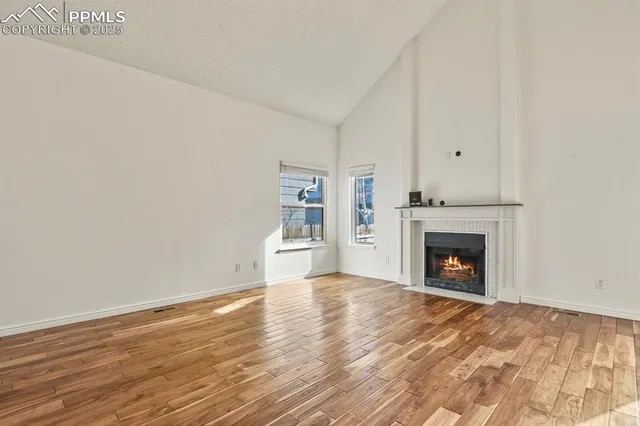 a view of an empty room with wooden floor fireplace and a window