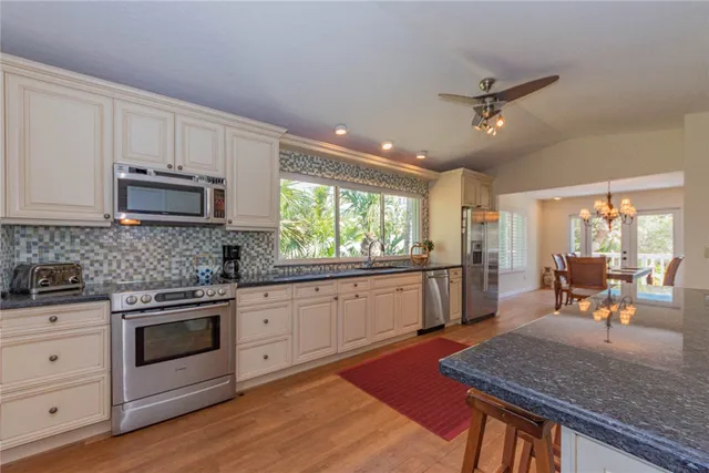 a kitchen with stainless steel appliances granite countertop wooden cabinets a stove a sink a dining table and chairs
