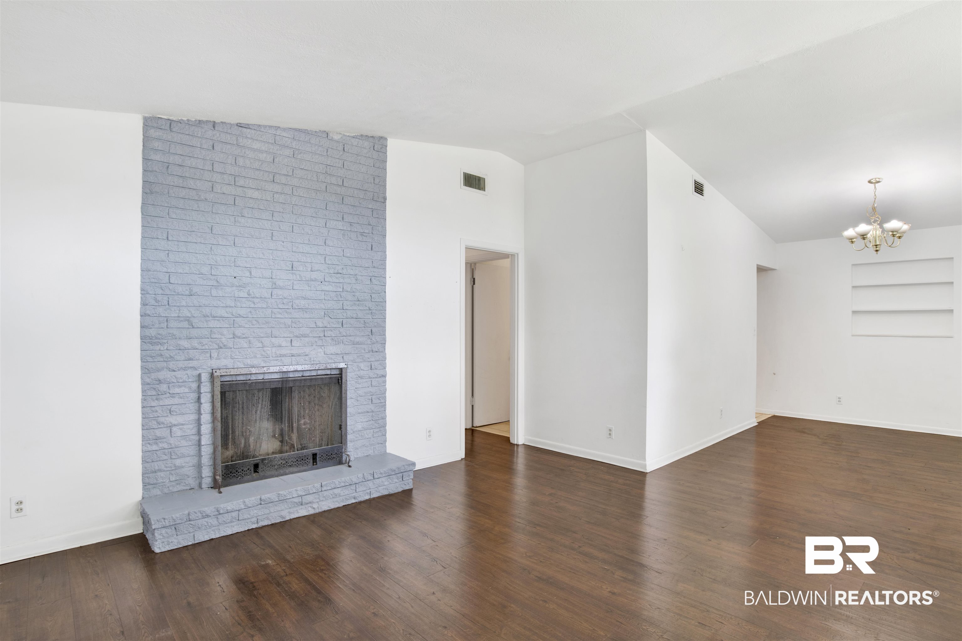 2 Lee Circle Daphne, AL 36527 - Photo 2 of 21 Unfurnished living room featuring a chandelier, brick wall, a fireplace, lofted ceiling, and wood-type flooring
