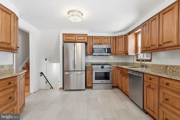 a kitchen with kitchen island granite countertop a stove top oven a sink dishwasher and a refrigerator with wooden cabinets