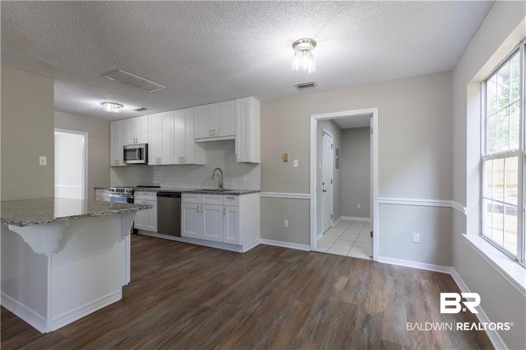 101 Lawson Road Daphne, AL 36526 - Photo 2 of 20 Open-concept kitchen featuring white shaker cabinetry, stainless steel appliances, granite-finish countertops, and wood-finish flooring