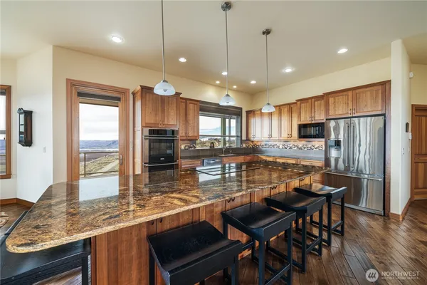 a kitchen with stainless steel appliances granite countertop a stove top oven a refrigerator a sink and chairs with wooden floor