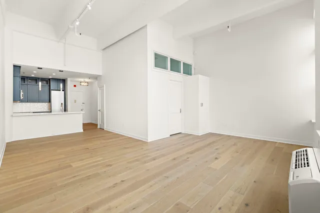 a view of empty room with wooden floor and kitchen view