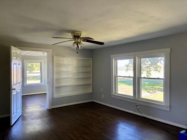 an empty room with wooden floor chandelier and windows