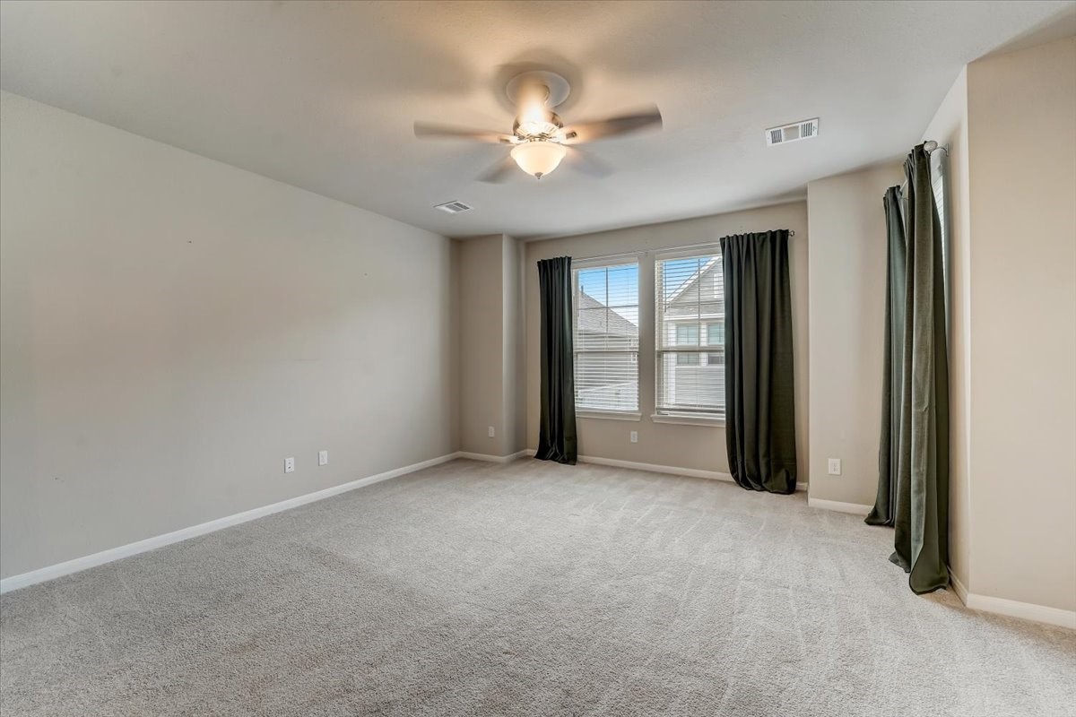 9438 Caddo Ridge Lane Cypress, TX 77433 - Photo 15 of 38 A spacious, well-lit bedroom with neutral walls and carpet. Features large windows, a bump out area for a seating space and a ceiling fan, offering a cozy and inviting atmosphere.