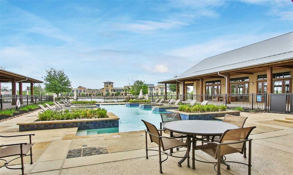 9438 Caddo Ridge Lane Cypress, TX 77433 - Photo 26 of 38 A community adults only pool area with a spacious patio, surrounded by lounge chairs and greenery. It features a modern clubhouse with large windows, providing an inviting space for relaxation and gatherings.