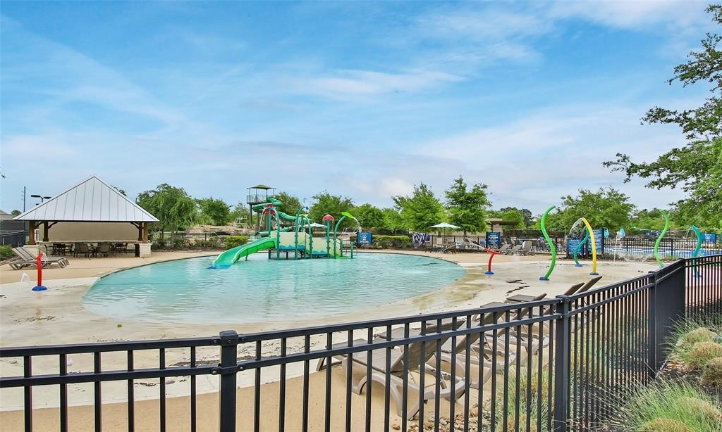 9438 Caddo Ridge Lane Cypress, TX 77433 - Photo 37 of 38 Splash pad and pool area, featuring water slides and play structures, ideal for family fun. The area is surrounded by a fence, with seating and a pavilion nearby, set in a landscaped environment.