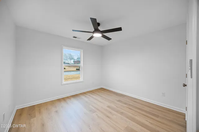 an empty room with wooden floor ceiling fan and windows