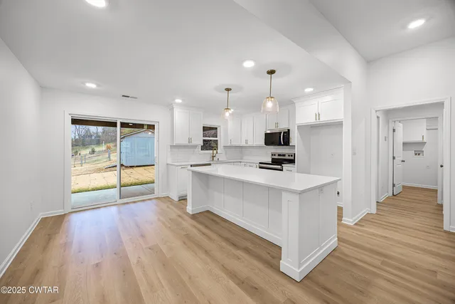 a large white kitchen with kitchen island a stove a refrigerator a sink dishwasher with wooden floor and cabinets next to a window