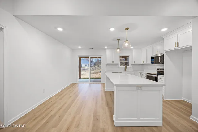 a large kitchen with stainless steel appliances granite countertop a stove a refrigerator a oven and white cabinets with wooden floor