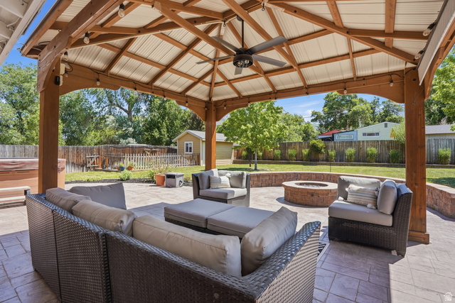 6889 South Village Road Salt Lake City, UT 84121 - Photo 27 of 44 Expansive outdoor living area featuring a vaulted gazebo with exposed wood beams and a ceiling fan, a stamped concrete patio, a built-in circular fire pit with a stone surround, string lighting, and a fenced perimeter