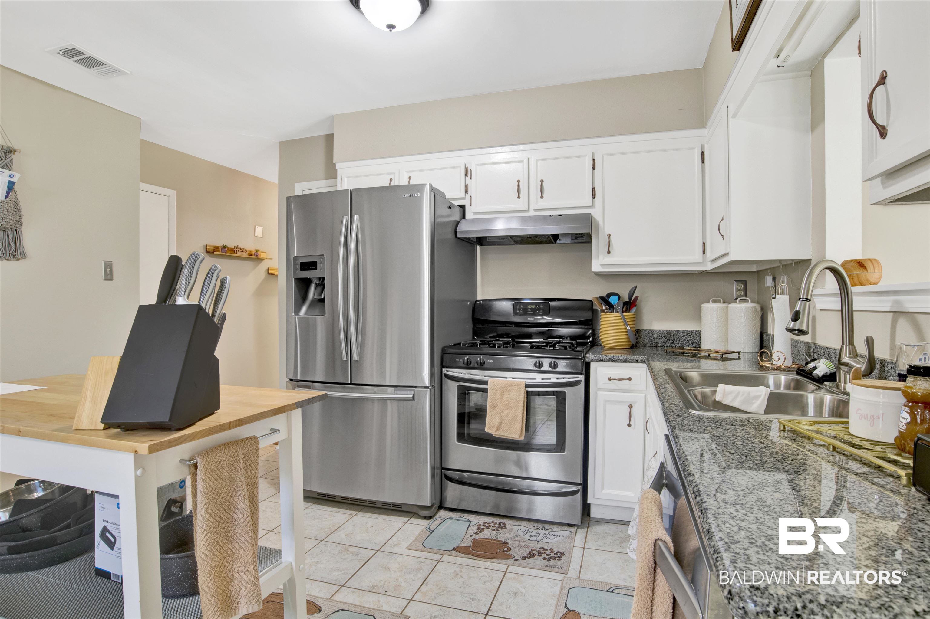 1476 Boudousquie Street Mobile, AL 36605 - Photo 9 of 34 Kitchen with appliances with stainless steel finishes, under cabinet range hood, white cabinets, light tile patterned flooring, and dark stone countertops