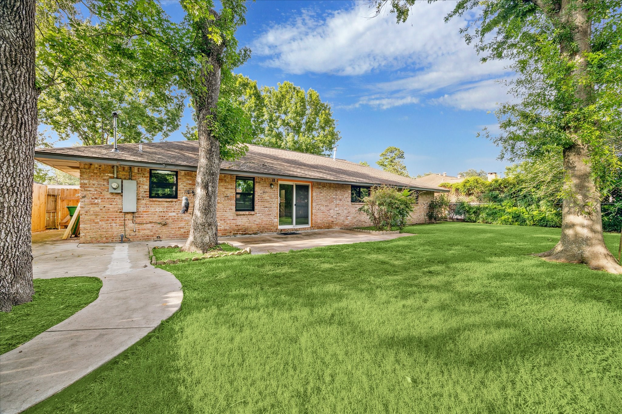 8907 Autauga Street Houston, TX 77080 - Photo 19 of 20 A charming brick home with a spacious backyard, lush green lawn, and mature trees. The property features a concrete path leading to a private back entrance, ideal for enjoying outdoor activities.