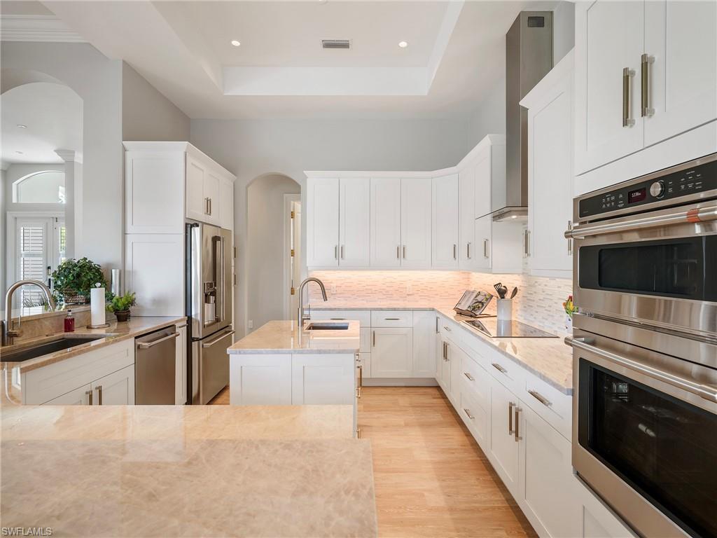 216 Springline Drive Naples, FL 34102 - Photo 23 of 46 Kitchen with stainless steel appliances, arched walkways, light stone counters, white cabinets, and a tray ceiling