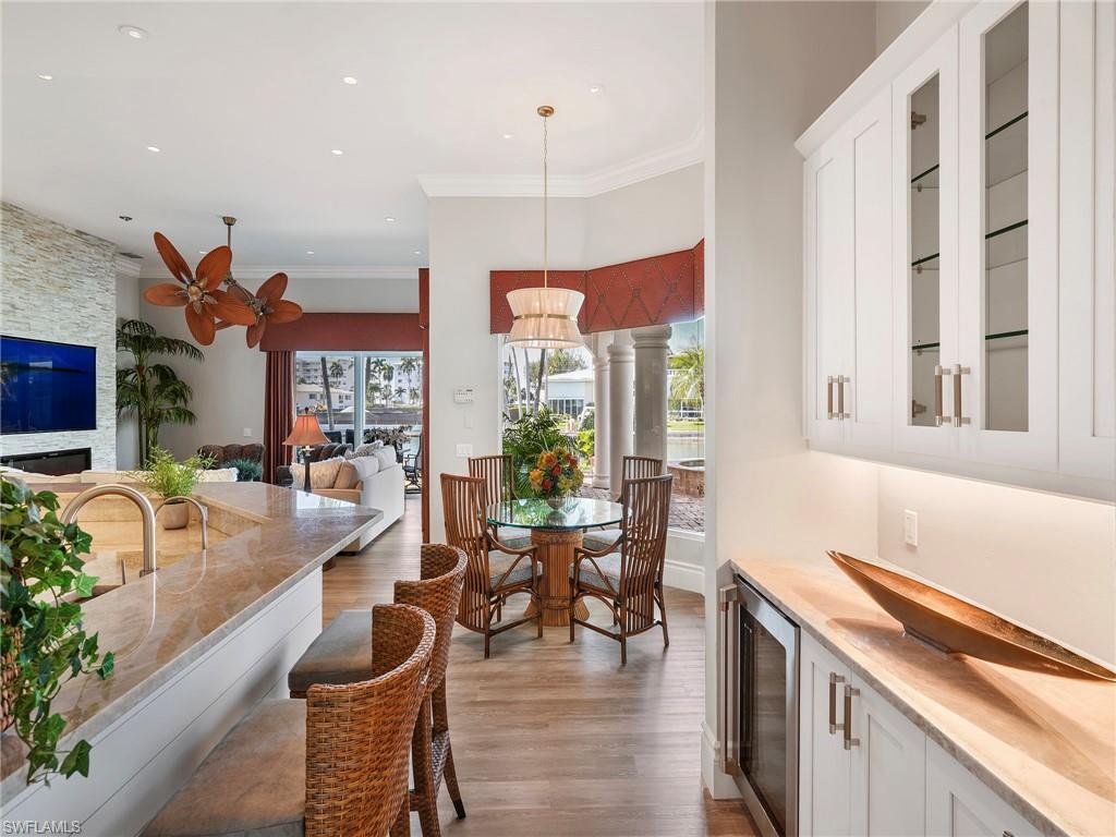 216 Springline Drive Naples, FL 34102 - Photo 26 of 46 Dining space with beverage cooler, crown molding, dark wood-type flooring, a stone fireplace, and recessed lighting