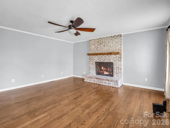 a view of an empty room with wooden floor fireplace and a window