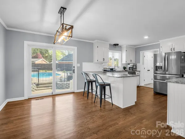 a kitchen with stainless steel appliances granite countertop a stove a refrigerator a microwave a dining table and chairs with wooden floor