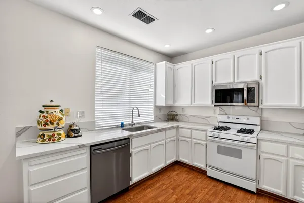 a white kitchen with a sink a stove and wooden floors