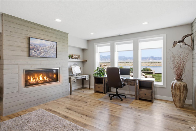21 Pier Place Tooele, UT 84074 - Photo 70 of 112 Spacious room featuring a horizontal plank accent wall with a built-in fireplace, light wood-finish flooring, and a wall of windows overlooking a body of water and distant mountains