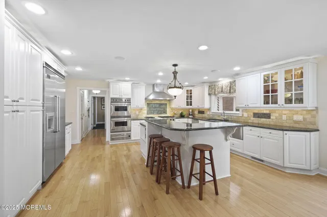 a kitchen with stainless steel appliances kitchen island granite countertop a stove a sink a refrigerator and white cabinets with wooden floor