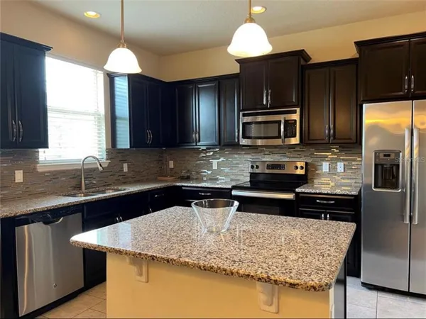 a kitchen with stainless steel appliances kitchen island granite countertop a sink a stove a dining table and chairs