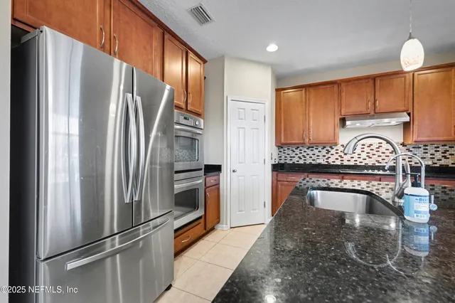 a kitchen with stainless steel appliances granite countertop a refrigerator a stove and a sink with wooden floor